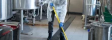 Profissional de uma empresa de limpeza industrial realizando higienização com equipamentos de segurança em ambiente fabril