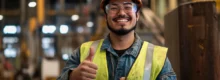 Trabalhador de indústria sorridente com capacete e óculos de proteção fazendo sinal de positivo, remetendo à NR-1 e saúde mental